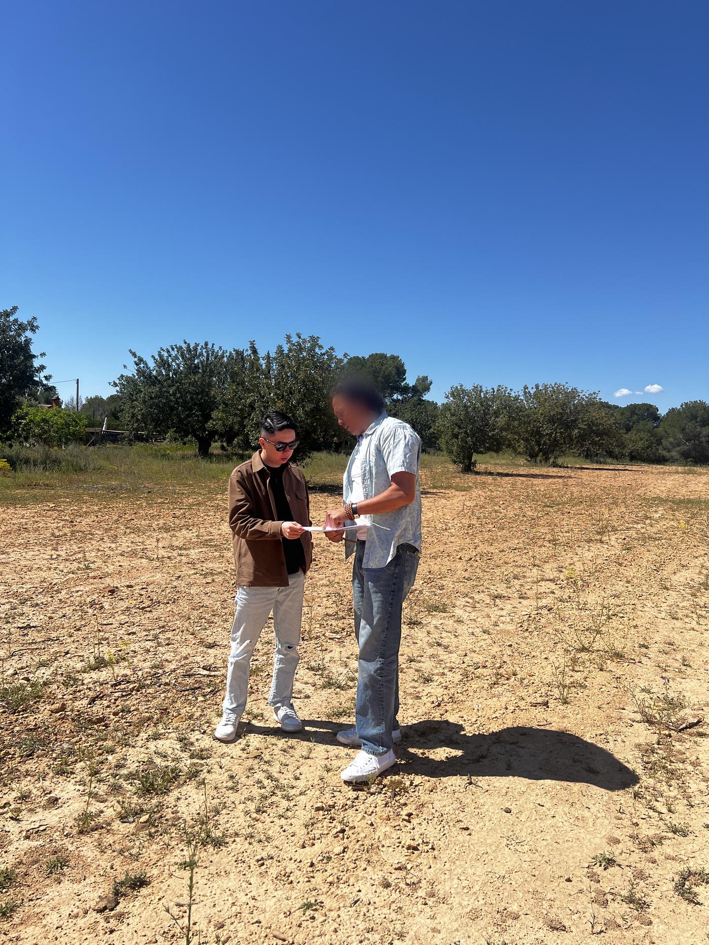 Daniel Siew and a project contact reviewing a document together on open, undeveloped land during an on-site Feng Shui assessment in Valencia, Spain.