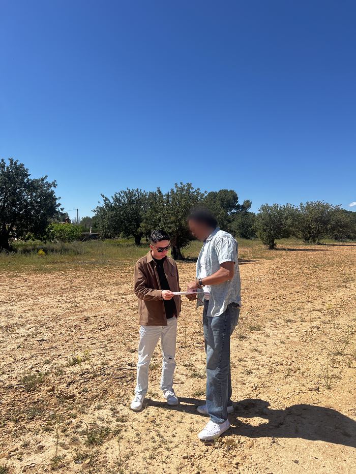 Daniel Siew reviewing paperwork with a project contact on open land bordered by trees in Valencia, Spain.