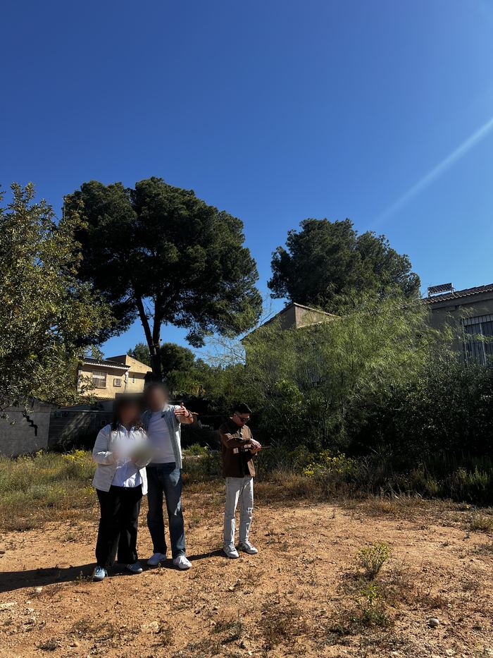 Daniel Siew taking notes on cleared land in Valencia, Spain, while two project contacts discuss the site.